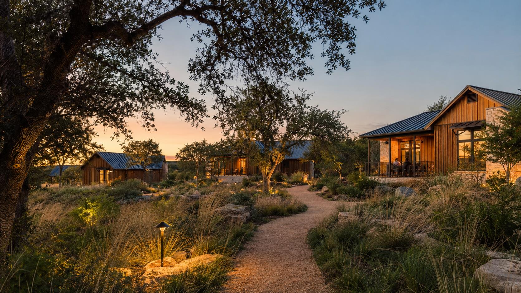 Guest cabins glowing at dusk along a lit gravel path beneath a live oak